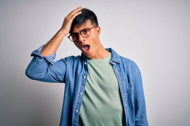 İzole edilmiş beyaz arka plan üzerinde gözlük ve tişört takan genç yakışıklı bir adam hata sonucu el ele tutuşarak şaşırdı, unutma. Unuttum, kötü hafıza konsepti.