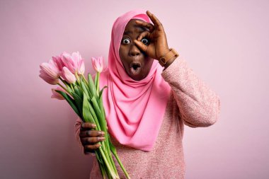 Genç Afro-Amerikan artı cüsseli kadın elinde pembe lale buketi tutan Müslüman kadın şaşırmış yüz ifadesiyle şaşırmış, parmaklarından içeri bakıyor. İnançsız ifade.