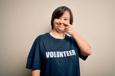 Sosyal yardım derneği tişörtü giyen genç Down sendromlu gönüllü kadın. El ve burunla işaret ediyor. Neşeli gülümsüyor. Güzellik konsepti