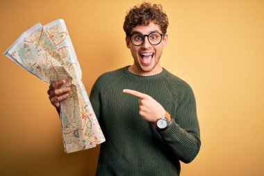 Sarı arka plan üzerinde kıvırcık saçlı, tatile çıkmış genç bir turist. El ve parmağıyla işaret ederek çok mutlu.