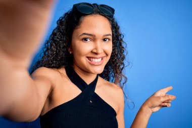 Kıvırcık saçlı, sıradan tişörtlü, fotoğraf makinesiyle selfie yapan genç ve güzel bir kadın.