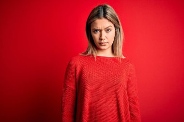 Genç ve güzel sarışın bir kadın, kırmızı izole edilmiş arka plan kuşkucu ve gergin üzerine sıradan bir süveter giyiyor, sorun yüzünden üzgün. Negatif kişi.