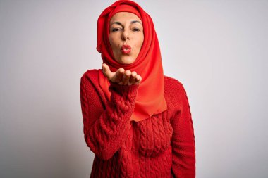 Orta yaşlı esmer kadın izole edilmiş beyaz arka plan üzerine geleneksel tesettür takmış kameraya bakıp havada öpücükler savuruyor güzel ve seksi. Aşk ifadesi.