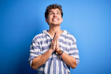 Sarışın, kıvırcık saçlı, sıradan çizgili kazak giyen, elleri bağlı yalvaran ve dua eden, yüzünde umut ifadesi olan çok duygusal ve endişeli genç bir adam. Yalvarıyorum..