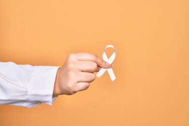 İzole edilmiş sarı arka planda beyaz kurdele tutan beyaz bir kadının eli