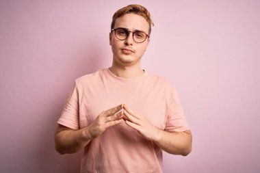 İzole edilmiş pembe arka plan üzerinde sıradan tişörtler giyen genç ve yakışıklı bir adam ellerini birleştirip gülümseyerek gevşemiş ve neşeli olmasını diliyordu. Başarı ve iyimser