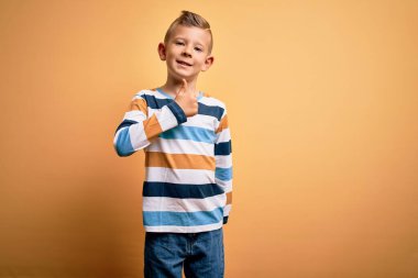 Küçük, beyaz, mavi gözlü, sarı arka plan üzerinde çizgili gömlek giyen, mutlu bir el hareketi yapan genç bir çocuk. Kameraya bakıp başarıyı gösteren ifade onaylanıyor.