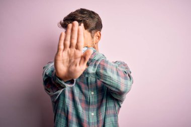Sakallı, sıradan bir gömlek giyen, pembe arka plan üzerinde duran, ellerle gözlerini kapayan, üzgün ve korku ifadeli hareketler yapan genç yakışıklı bir adam. Utanç verici ve olumsuz bir kavram..