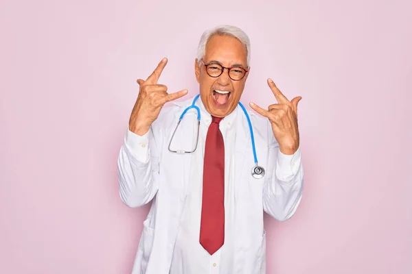 手でロックシンボルをやって狂気の表情で叫んで聴診器とプロの医療コートを身に着けている中世のシニア白髪の医師の男 音楽スター 重い音楽の概念 — ストック写真