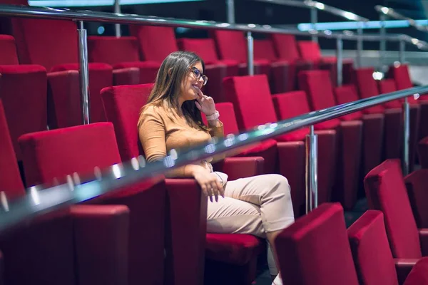 若い美しい女性が幸せと自信を笑顔 劇場で笑顔で赤い椅子に座って — ストック写真