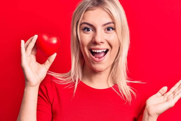 Young Beautiful Blonde Woman Holding Plastic Heart Standing Isolated Red — Stock Photo, Image