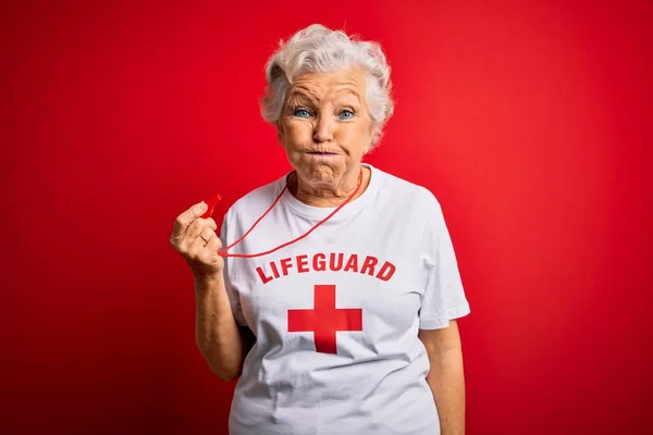 年长美丽的灰白头发的救生员女人穿着印有红十字图案的T恤衫 面容滑稽 吹口哨 满嘴通气 满嘴疯狂的表情 — 图库照片