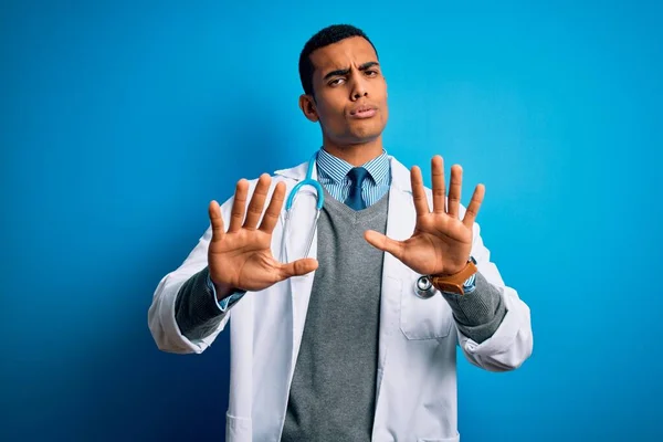 英俊的非洲裔美国医生 身穿外套 头戴听诊器 头戴蓝色背景 双手移开 带着恐惧和恶心的表情 表示拒绝和否认 停止和禁止 — 图库照片