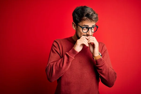 Sakallı Gözlüklü Süveterli Genç Bir Adam Kırmızı Arka Planda Dikiliyor — Stok fotoğraf
