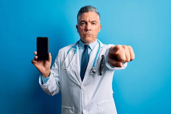 中年英俊的白发苍苍的医生手持智能手机 用手指指向相机和你 正面做出积极自信的手势 — 图库照片