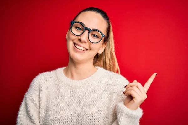 美丽的金发女人 蓝眼睛 身穿毛衣 戴着眼镜 脸上挂着大大的笑容 手和手指指向侧面看相机 — 图库照片