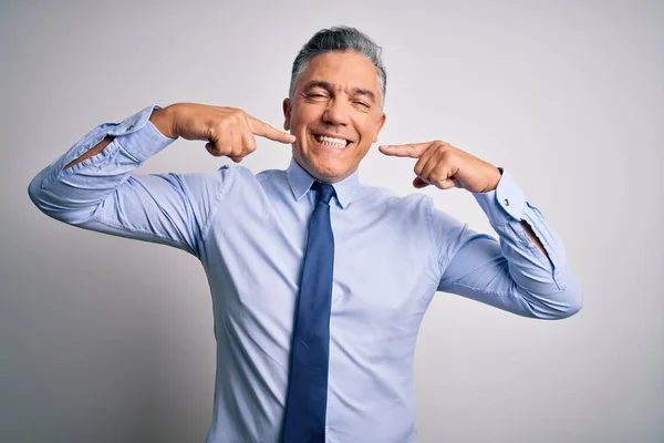 Middle age handsome grey-haired business man wearing elegant shirt and tie smiling cheerful showing and pointing with fingers teeth and mouth. Dental health concept.