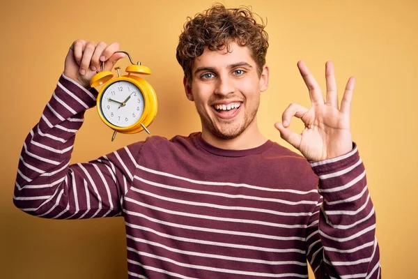 Jovem Loiro Com Cabelo Encaracolado Segurando Despertador Sobre Fundo Amarelo — Fotografia de Stock