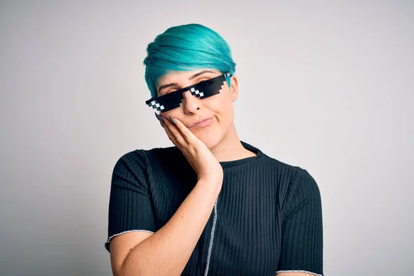 Young woman with blue fashion hair wearing thug life sunglasses over white background thinking looking tired and bored with depression problems with crossed arms.