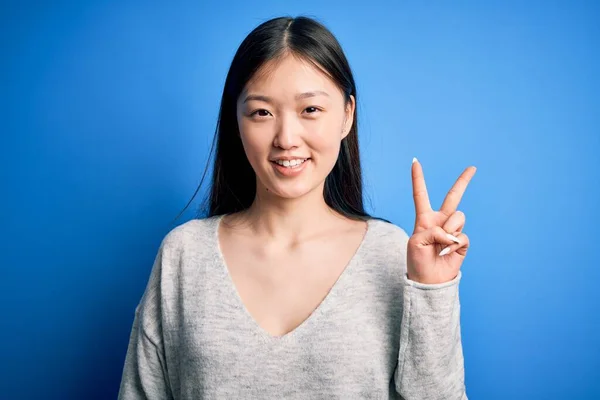 Młoda Piękna Azjatycka Kobieta Ubrana Luźny Sweter Stojąca Nad Niebieskim — Zdjęcie stockowe