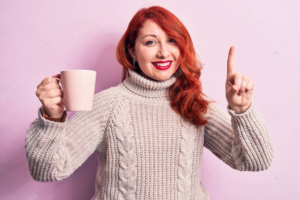 Young beautiful redhead woman drinking cup of coffee over isolated pink background smiling with an idea or question pointing finger with happy face, number one