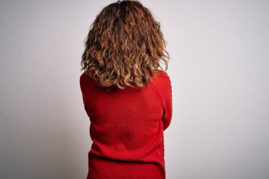 Orta yaşlı esmer kadın, sıradan bir süveter giyiyor, izole edilmiş beyaz arka planda dikiliyor, geriye bakıyor ve kollarını kavuşturuyor.