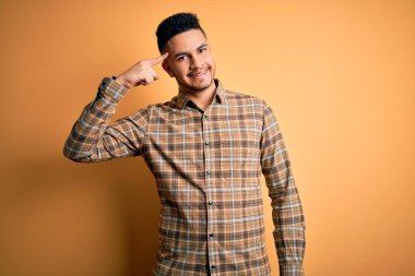 Sarı arka plan üzerinde duran rahat tişörtlü genç yakışıklı adam tek parmakla kafasını işaret ediyor, harika bir fikir ya da düşünce, iyi bir hafıza.