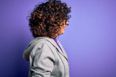 Güzel kıvırcık Arap sporcu kadın spor yapıyor. Mor arka planda spor kıyafetleri giyiyor. Yan tarafa bakıyor..