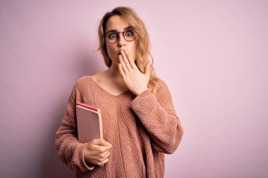 Genç, sarışın, gözlüklü, pembe arka plan kapağı üzerinde not defteri tutan bir kadın. Ağzı açık, utancından ağzı açık, korku ifadesi. Sessizlikten korkan, gizli bir konsept.