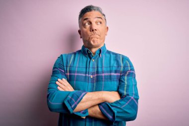 Orta yaşlı, yakışıklı, gri saçlı, rahat bir gömlek giyen, pembe arka planda yaşayan, gülümseyen ve kafasını çeviren bir adam..