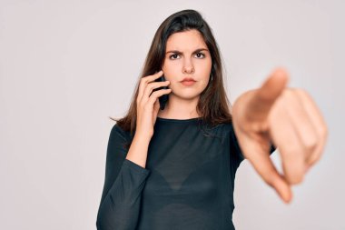 Akıllı telefondan konuşan genç güzel bir kadın izole edilmiş arka planda kamerayı işaret ediyor ve sen, el işareti, ön taraftan pozitif ve kendinden emin bir hareket.