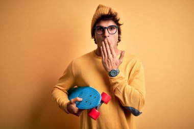 Genç ve yakışıklı bir öğrenci, sarı arka planda gözlük takıyor. Ağzı kapalı, elleri utançla kaplı. Yanlışlıkla şok olmuş, korkunun ifadesi.