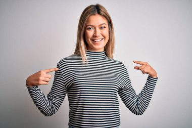 İzole edilmiş arka plan üzerinde sıradan çizgili süveter giyen genç ve güzel sarışın bir kadın. Kendine güvenen, yüzünde bir gülümsemeyle kendini gururlu ve mutlu bir şekilde gösteren biri..