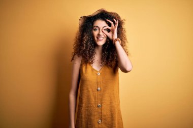 Güzel esmer kadın tatilde. Kıvırcık saçlı ve piercing takıyor. Şapka ve elbise giyiyor..