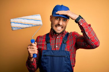 Duvarı boyayan genç yakışıklı ressam, izole edilmiş sarı arka planda paten kullanıyor. Elleri başının üstünde, utanç ve şaşkınlık dolu, sinirli ve hayal kırıklığına uğramış bir halde. Hata için korku ve üzüntü.