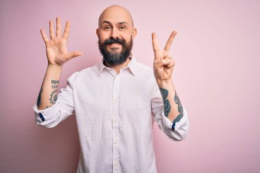 Sakallı yakışıklı, zarif bir gömlek giyen, pembe arka planda gezen, 7 numaralı parmaklarını gösterip gülümseyen, kendinden emin ve mutlu bir adam..
