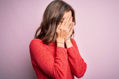 Pembe izole edilmiş arka planda genç, güzel sarışın bir kız. Ağlarken yüzünü ellerle kapatan üzgün bir yüz ifadesi var. Depresyon kavramı.