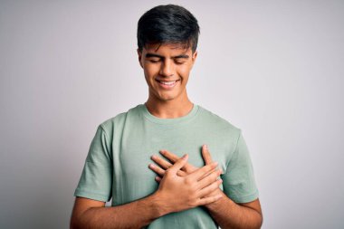 İzole edilmiş beyaz arka plan üzerinde sıradan bir tişört giyen, elleri göğsünde, gözleri kapalı ve yüzünde minnet dolu bir jest olan genç yakışıklı bir adam. Sağlık kavramı.