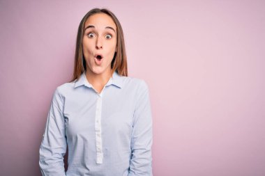 Zarif bir tişört giyen genç ve güzel bir iş kadını pembe arka planda korkmuş ve şok olmuş bir şekilde duruyor..