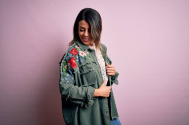 Moda kıyafetleri giyen genç ve güzel bir kadın. Manken, sokak tarzı giyiniyor. Pembe arka planda dikiliyor.