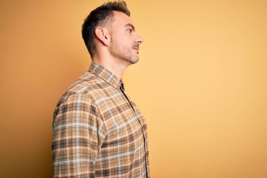 Sarı arka plan üzerinde duran, rahat bir görünüm veren, kendine güvenen bir gülümsemeye sahip genç ve yakışıklı bir adam..