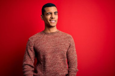 Genç, yakışıklı, Afro-Amerikalı bir adam kırmızı arka planda dikilmiş kameraya seksi bir ifadeyle bakıyor, neşeli ve mutlu bir yüz..