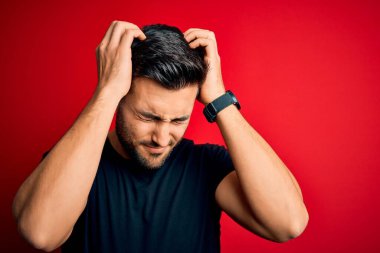 Genç, siyah bir tişört giyen yakışıklı adam izole edilmiş kırmızı arka planda dikiliyor. Ağrı ve migren yüzünden baş ağrısı ve stresten muzdarip. Ellerini başının üstüne koy..