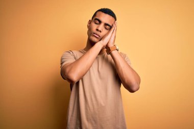 Genç, yakışıklı, Afro-Amerikalı bir adam. Günlük tişört giyiyor. Sarı arka plan üzerinde duruyor..