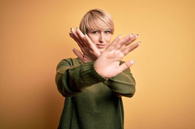 Sarışın, modern kısa saçlı, sarı arka planda rahat süveter giyen genç bir kadın.