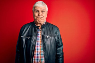 Kıdemli yakışıklı, beyaz gömlekli ve ceketli adam izole edilmiş kırmızı arka planda komik yüzlü, şişkin yanaklar. Havayla şişmiş ağız, çılgın bir ifade..