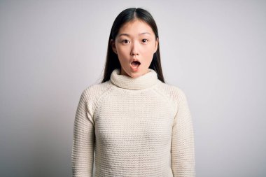 Genç, güzel Asyalı kadın rahat bir süveter giyiyor. Arka planda duruyor. Korkmuş ve şok olmuş bir halde..