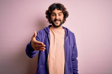 Genç, yakışıklı, sakallı, pembe arka planda rahat bir tişört giyen, dostça gülümseyerek selamlaşan, hoş geldin diyen bir adam. Başarılı bir iş..