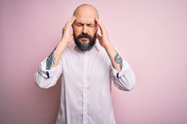Sakallı, zarif gömlekli yakışıklı, pembe arka planda, başı ağrıyan bir adam. Çünkü stres var. Migren ağrısı..
