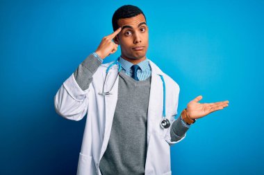 Mavi arka plan üzerinde steteskop ve ceket giyen yakışıklı Afro-Amerikan doktor. Kafası karışmış ve avuç içi açık bir şekilde fotokopi alanı göstermekten rahatsız olmuş ve alnını işaret ediyor. Bunu bir düşün..